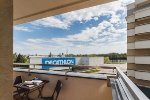 A cozy balcony with chairs and a table, showing a view that includes a Decathlon store in the background.