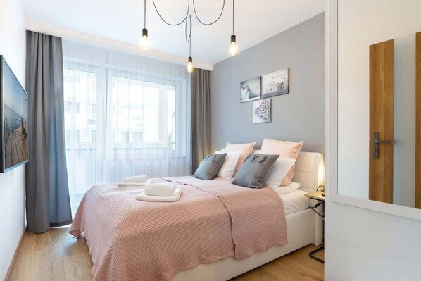 A cozy bedroom with a soft color palette. It has a large bed with blush pink bedding, light-colored curtains, and wall art for added elegance.