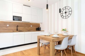 A compact kitchen and dining area with white cabinetry and a small dining table. A black accent clock and pendant lights add style.