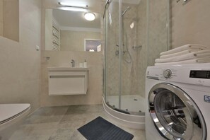 A compact bathroom with a glass shower enclosure, sink, and a washing machine for added convenience.