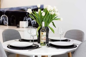 A dining area with a round table set with stylish dinnerware, including wine glasses and a flower vase.