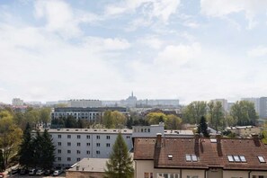 A scenic view of the city from the balcony, showing nearby rooftops and greenery in the distance.