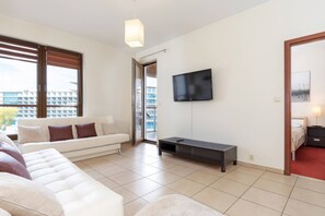 A bright living room with a comfortable white sofa, a coffee table, and a mounted flat-screen TV, creating a relaxing area to unwind.