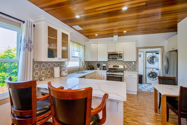 Kitchen with bar stools, gas stove, microwave oven,  small dinning table.