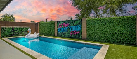 Private backyard oasis featuring a heated sparkling blue pool, fun mural, sun loungers, covered patio, outdoor dining and a firepit!