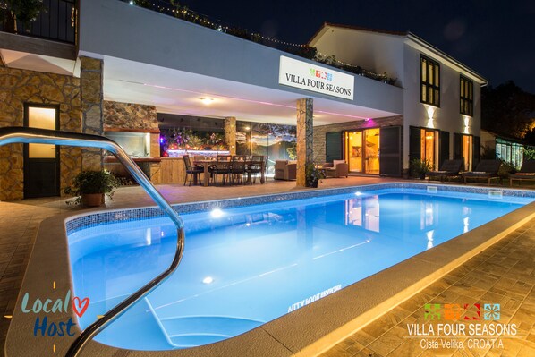 Outdoor area with swimming pool, BBQ, covered and open terrace at night.