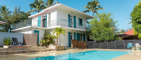 Villa vue de la piscine avec espace repas à l'ombre des manguiers à droite