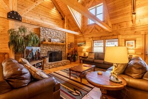 Living Room with Stacked Stone Fireplace, Large Flatscreen TV, and Exposed Beam High Vaulted Ceilings