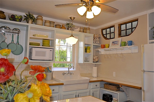 Bright charming coastal kitchen with farm sink. Antique windows over shelf.