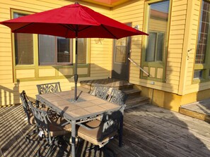 A large deck boasts a gas BBQ, large dining table + chairs with an umbrella.