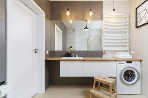 Modern bathroom with white cabinets, wooden countertop and washing machine. 
