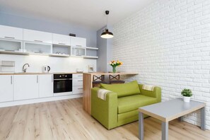 Living room with green sofa connected to kitchenette. 