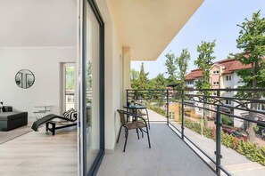  Modern balcony with outdoor seating, overlooking a street lined with trees. The railing is sleek and black.