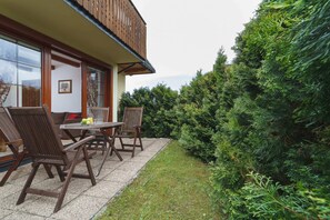 An outdoor seating area with a table and chairs set on a terrace overlooking a garden and the surrounding greenery.