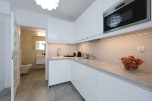 A sleek kitchenette with white cabinetry, integrated appliances, and under-cabinet lighting.