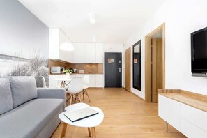 Another angle of the living room, showing a grey sofa, a coffee table, and a TV mounted on a white stand.