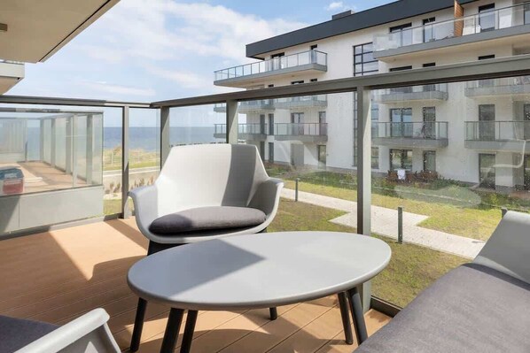 A balcony view with a round table and two white chairs, overlooking the modern apartment complex and a green courtyard.