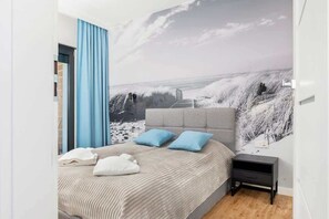 A bedroom with a cozy double bed, light bedding, and a wall decorated with a large picture of a snowy mountain landscape.