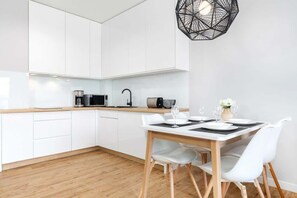 A sleek kitchenette with white cabinets and a wooden countertop, connected to a dining area with a round table and white chairs.