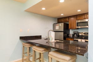 Fully equipped kitchen with stainless steel appliances and breakfast bar that seats three