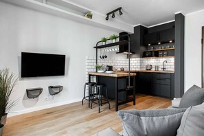 A spacious living room with a large couch facing a wall-mounted TV. There are open shelves on the wall, and the design feels modern with an industrial touch.