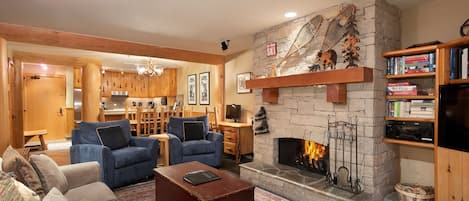 Lounge features a stone-surround presto log fireplace, TV, and sliding door access to the deck