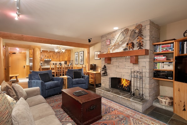 Lounge features a stone-surround presto log fireplace, TV, and sliding door access to the deck