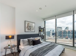 A modern and well-lit bedroom featuring a plush queen bed, built-in wardrobes with floor-to-ceiling mirrors and bedside tables