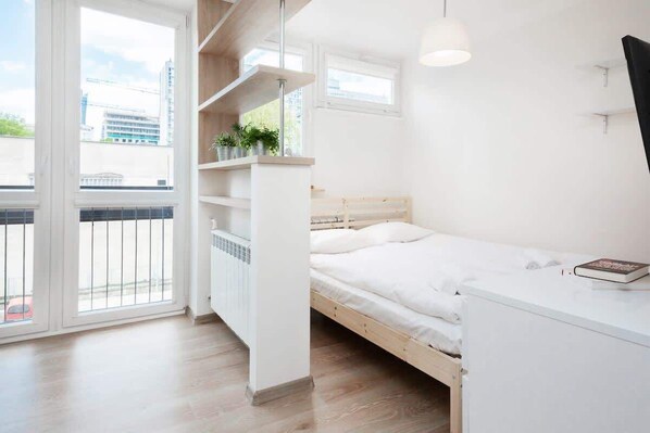 A close-up of the double bed with soft bedding, showing its placement by a bright window.