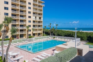 Resort-style outdoor heated pool surrounded by palm trees and a bright blue sky.
