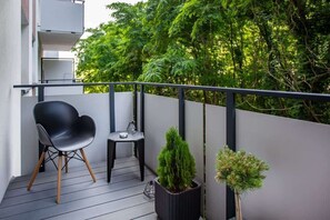 A private balcony with chairs, a small table, and potted plants, offering a serene outdoor space surrounded by lush greenery.