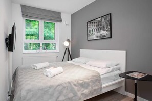 A cozy bedroom with a minimalist design, featuring a neatly made bed, a TV on the wall, and a small side table, providing a peaceful space for relaxation.