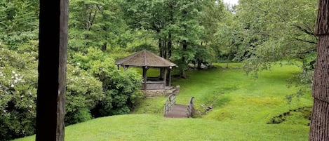View from covered porch of bridge crossing creek to gazebo, pond and fire pit.  