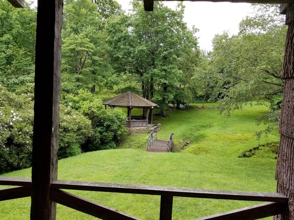 View from covered porch of bridge crossing creek to gazebo, pond and fire pit.  