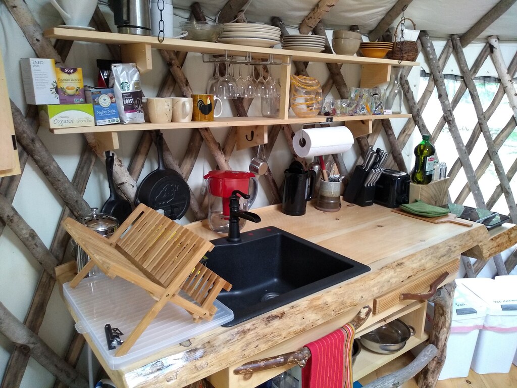 A rustic countertop in a Maine glamping yurt has glassware, a sink, and other cooking necessities visible