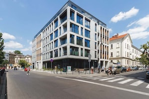 An exterior view of a contemporary building on a street corner. The structure features large glass windows and a clean, geometric design.