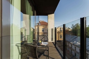 A view of a balcony space, featuring glass railing and outdoor seating. The cityscape is visible in the background, giving a sense of open space.
