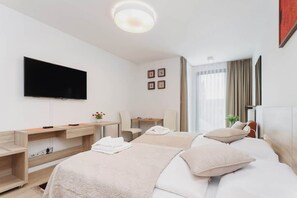 A similar bedroom setup with a wide-angle view, showcasing the double bed, a TV mounted on the wall, and a small desk area. The space looks inviting and comfortable.