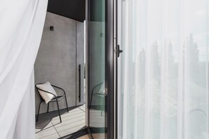 A balcony with a small table and two black chairs, enclosed by a glass railing. The view overlooks the city, offering a peaceful outdoor space.