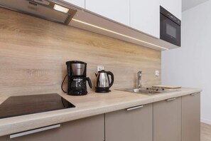A kitchenette with light-colored cabinets, a microwave, a coffee maker, and a kettle. The design is simple and functional, with easy access to cooking essentials.
