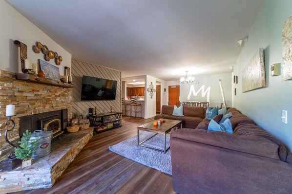 Open living area with luxury vinyl flooring throughout. Large flatscreen TV w/ smart features and wood burning fireplace.