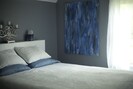 Master bedroom with queen- sized platform bed, cotton damask duvet, luxurious sheets and plump feather-free pillows. There is one full-sized window adorned with a shear curtain.