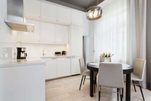 A wider view of a kitchen combined with a small dining area. It features white cabinets, a dining table, and a few decorative plants.