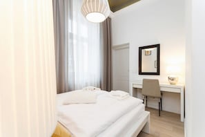 A cozy bedroom with a double bed and a small desk with a chair, perfect for working or studying. The room is bright with minimal decor.