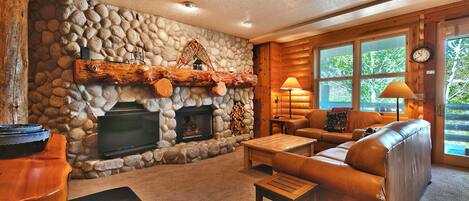 Spacious living room with feature river stone fireplace wall, flat screen TV, and stunning single log mantle