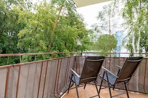 A cozy balcony with a small table and two chairs. It overlooks a green, leafy view, offering a relaxing outdoor space.