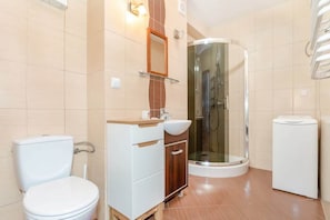 A clean, tiled bathroom with a shower cabin, toilet, and sink. The space is well-lit and practical.