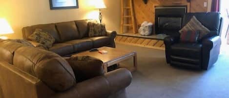 The cozy living area is full of classic cabin charm and ample plush seating between two couches, a coffee and a comfortable recliner, all surrounding the striking wood-paneled fireplace.