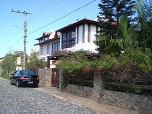 Fachada desde a rua do condomínio e muro com cerca.