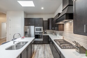 Side View of Kitchen - The kitchen is fully stocked with all the dishes, cookware, baking pans, and cutlery you will need for meal preparations and includes stainless steel appliances and quartz counter tops.